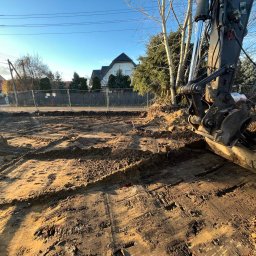 Budomad Michał Domagała - Przygotowanie terenu pod budowę domu: wykopany fundament z widocznym fragmentem koparki i ogrodzeniem placu budowy w tle.