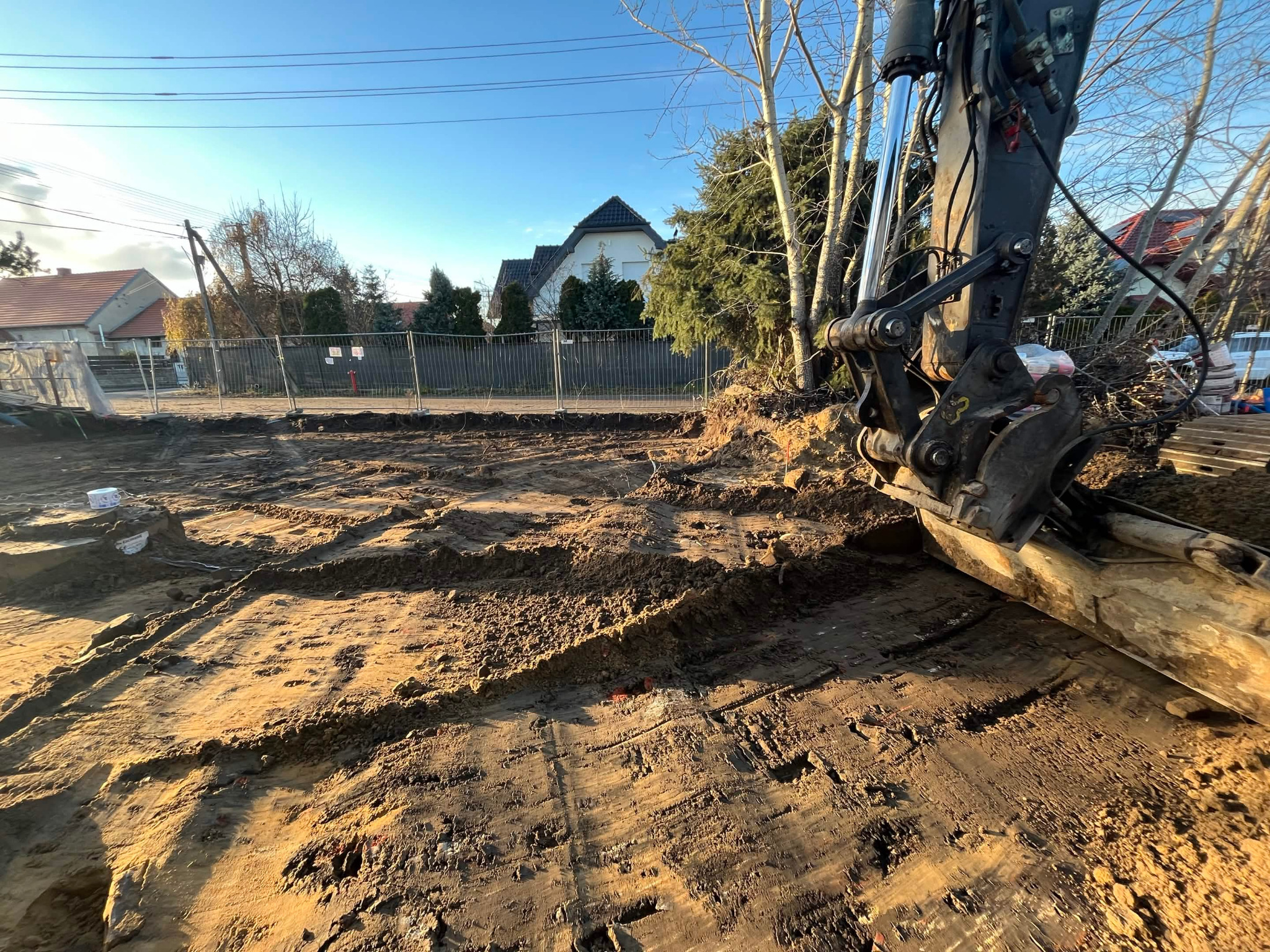 Przygotowanie terenu pod budowę domu: wykopany fundament z widocznym fragmentem koparki i ogrodzeniem placu budowy w tle.