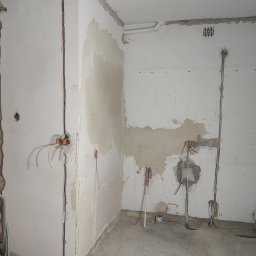 GLUVOLT Michał Głuchy - Wnętrze w trakcie remontu: odsłonięte instalacje elektryczne w ścianach, widoczne puszki i przewody. Fragmenty ścian z resztkami starej farby i tynku. Stan surowy.