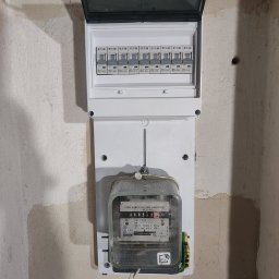 GLUVOLT Instalacje Elektryczne i Remonty - Otwarta skrzynka z bezpiecznikami i licznikiem energii elektrycznej na surowej ścianie. Widoczne bezpieczniki EATON i licznik PRL T3195.