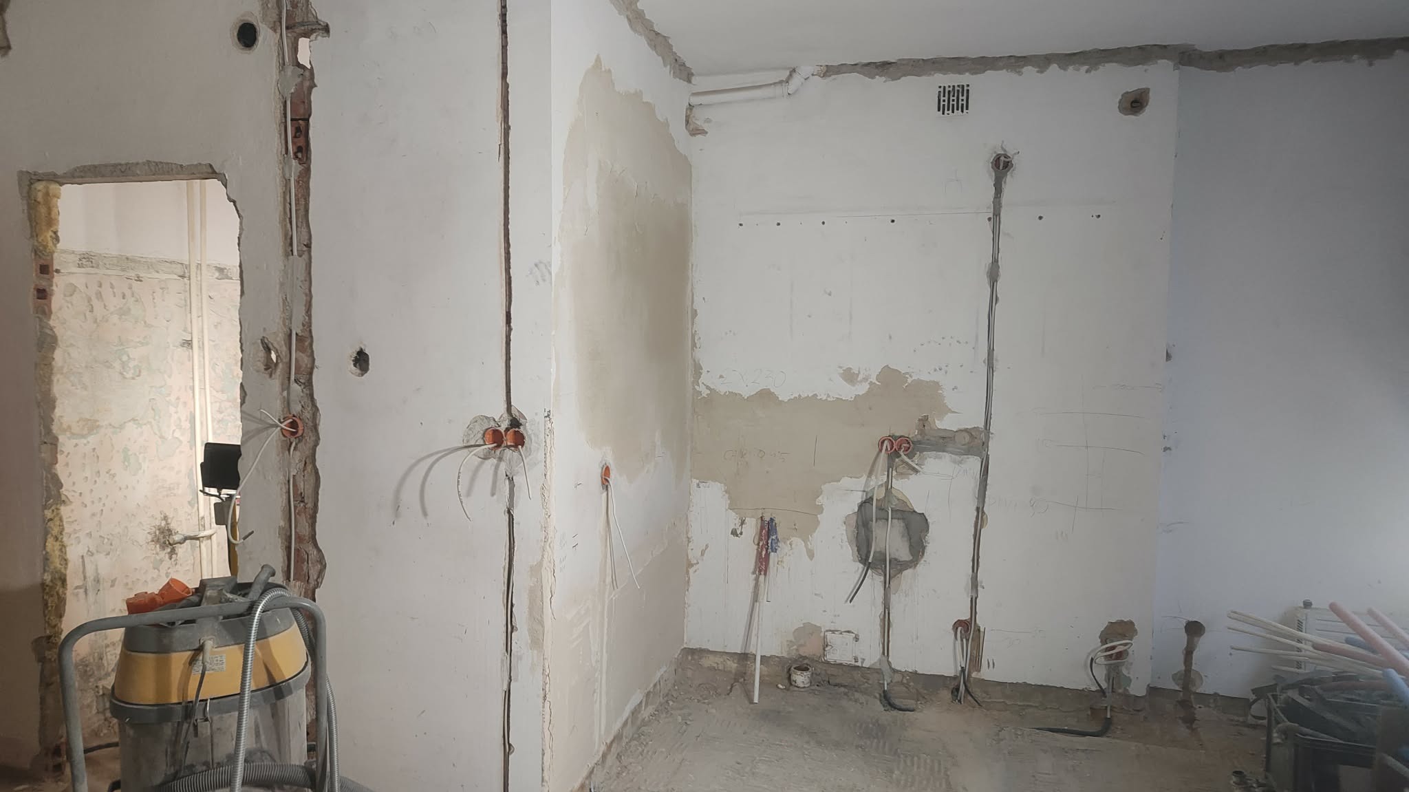 Wnętrze w trakcie remontu: odsłonięte instalacje elektryczne w ścianach, widoczne puszki i przewody. Fragmenty ścian z resztkami starej farby i tynku. Stan surowy.