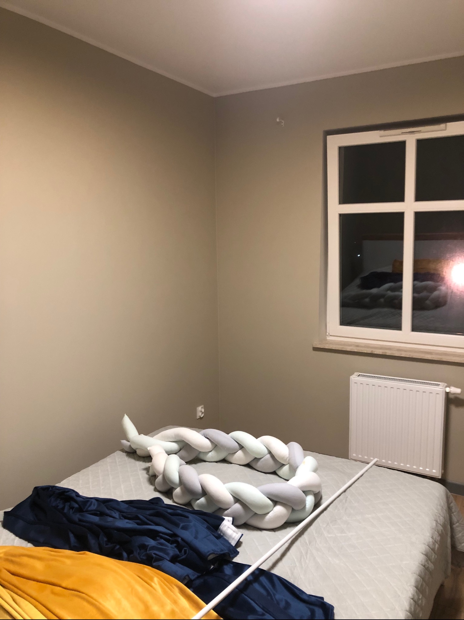 Pokój po malowaniu ścian na beżowo, widoczne okno z grzejnikiem, łóżko z ozdobnym warkoczem i pościelą. Ściany świeżo pomalowane, brak śladów niedociągnięć.