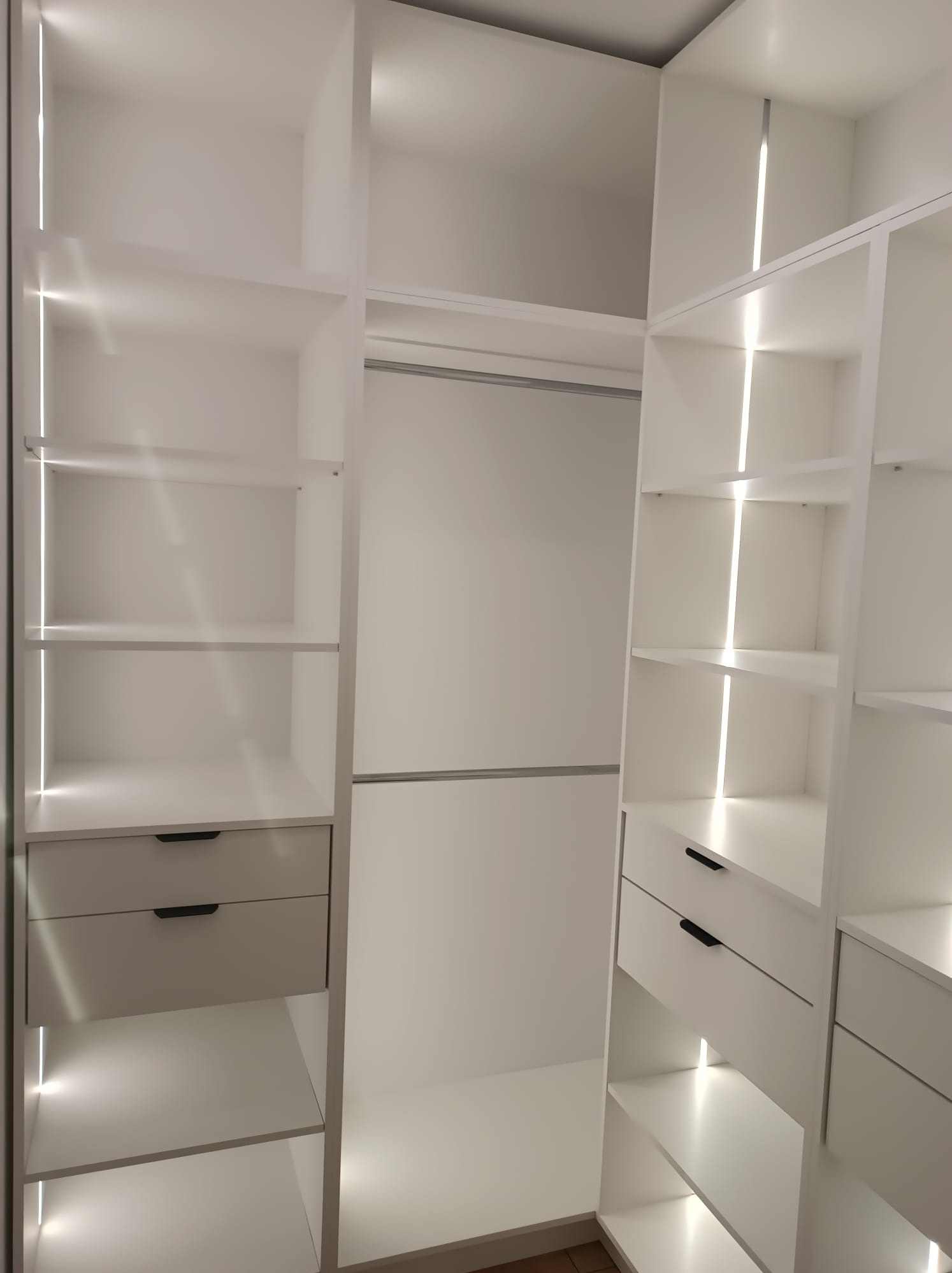 Biała, nowoczesna szafa wnękowa z oświetleniem LED, widok z wnętrza. Półki i szuflady z minimalistycznymi uchwytami. Jasne, neutralne tło.