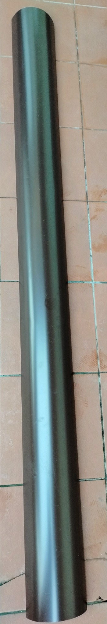 Brązowa, metalowa rynna dachowa leżąca na pomarańczowych płytkach. Widoczne odbicie światła na powierzchni rynny.