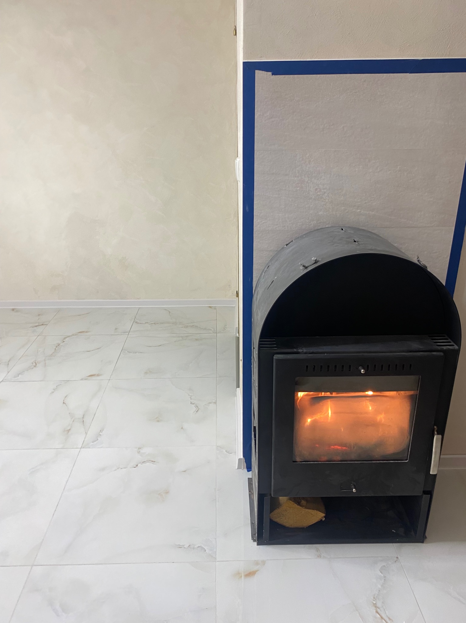 Nowoczesny kominek w jasnym wnętrzu z marmurową podłogą i świeżo pomalowanymi ścianami. Widoczne detale wykończenia i przygotowania do montażu.