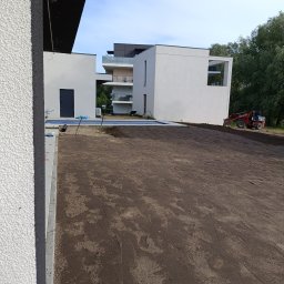 Teren Zieleni Vasyl Dutchak - Przygotowanie terenu pod trawnik na posesji z nowoczesnym budynkiem. Widoczna rozplantowana ziemia, miniładowarka i elementy instalacji nawadniającej.