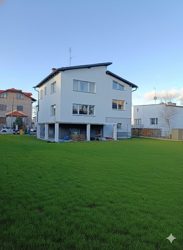 Dwupiętrowy dom z białymi ścianami i zielonym trawnikiem. Widoczne podpory pod budynkiem. Ujęcie z niskiej perspektywy podkreśla przestrzeń trawnika.