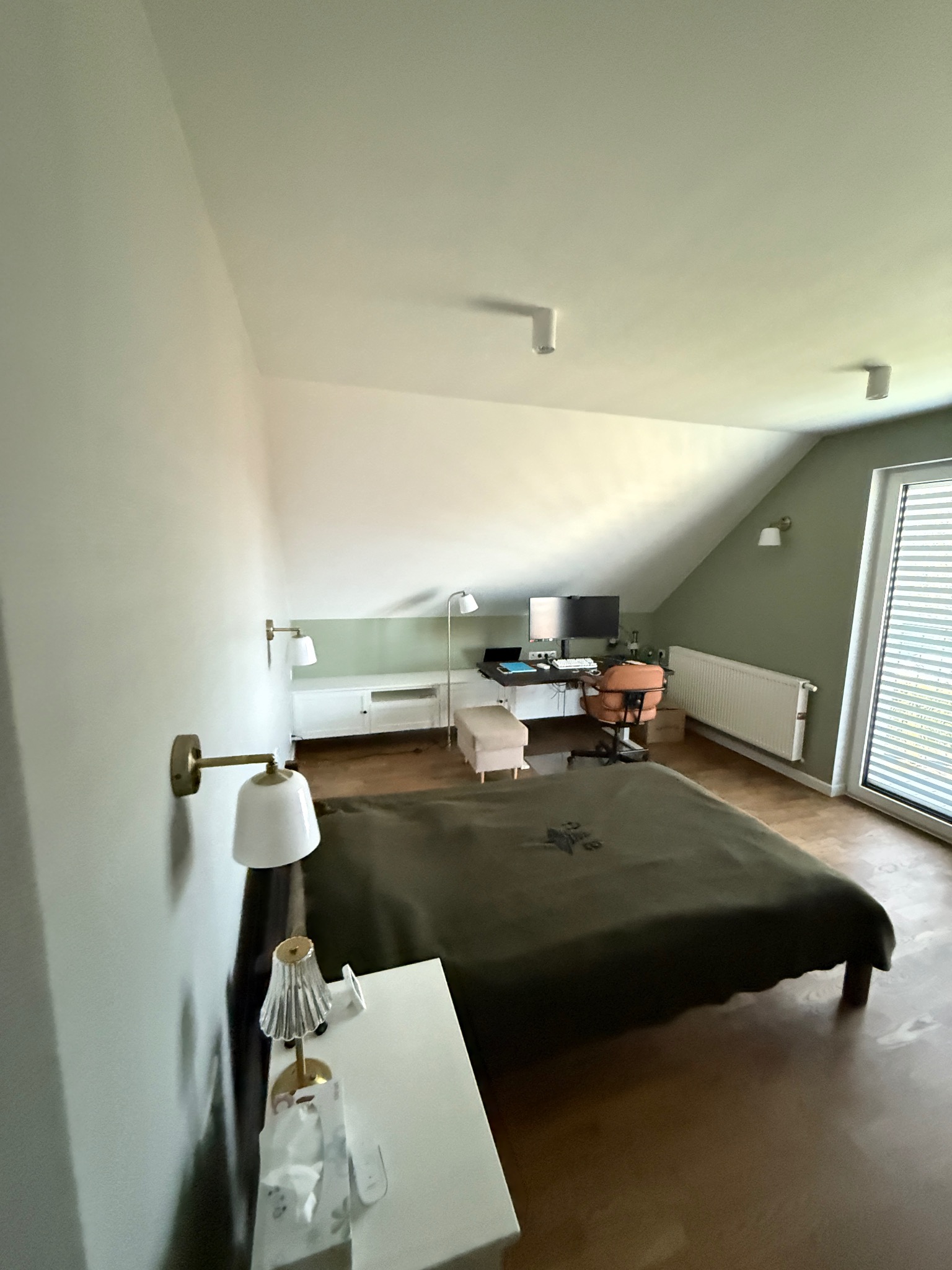 Pokój na poddaszu z łóżkiem, biurkiem i oknem. Ściany pomalowane na biało i zielono. Widoczne lampki nocne i biurkowe. Ustawienie mebli w pokoju.