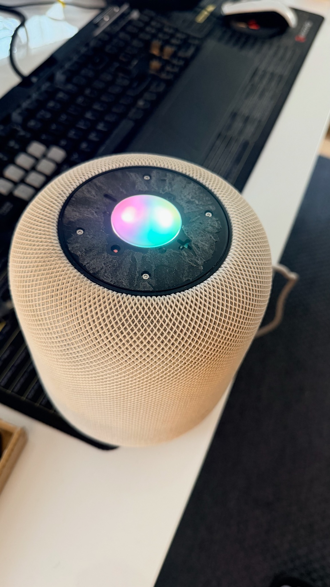 Głośnik inteligentny z podświetleniem RGB na biurku obok klawiatury. Widoczne ślady użytkowania na górnej części urządzenia. Bliskie ujęcie.