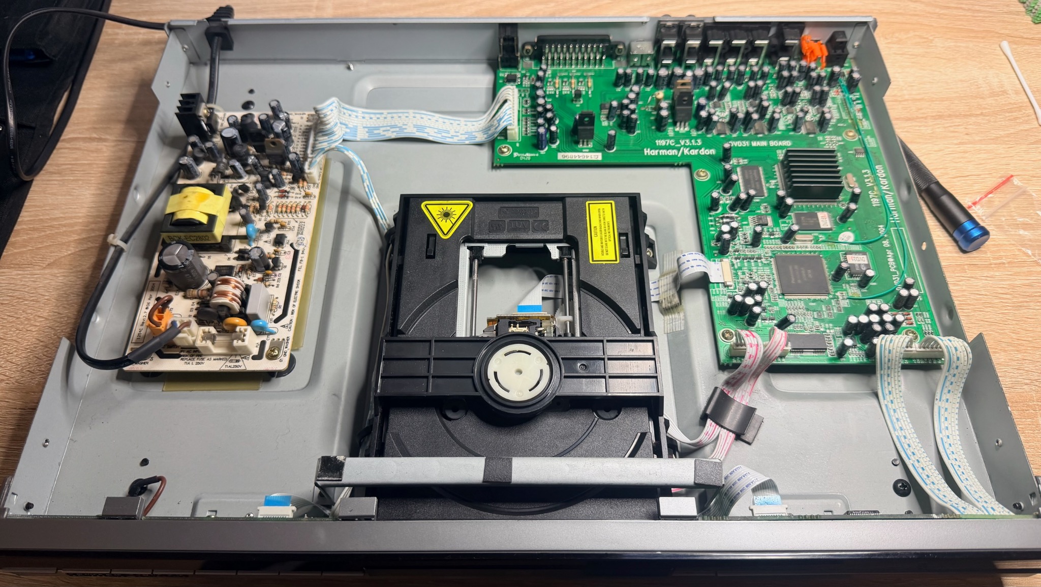 Otwarty odtwarzacz CD Harman/Kardon w trakcie naprawy. Widoczne układy scalone, płyta główna i mechanizm lasera. Precyzyjna praca serwisowa.