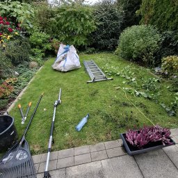 Green Alley Krzysztof Tarasiewicz - Uporządkowany trawnik po przycinaniu, z narzędziami ogrodniczymi, workiem na odpady i drabiną. Widoczne kwiaty w donicy i starannie utrzymana zieleń.