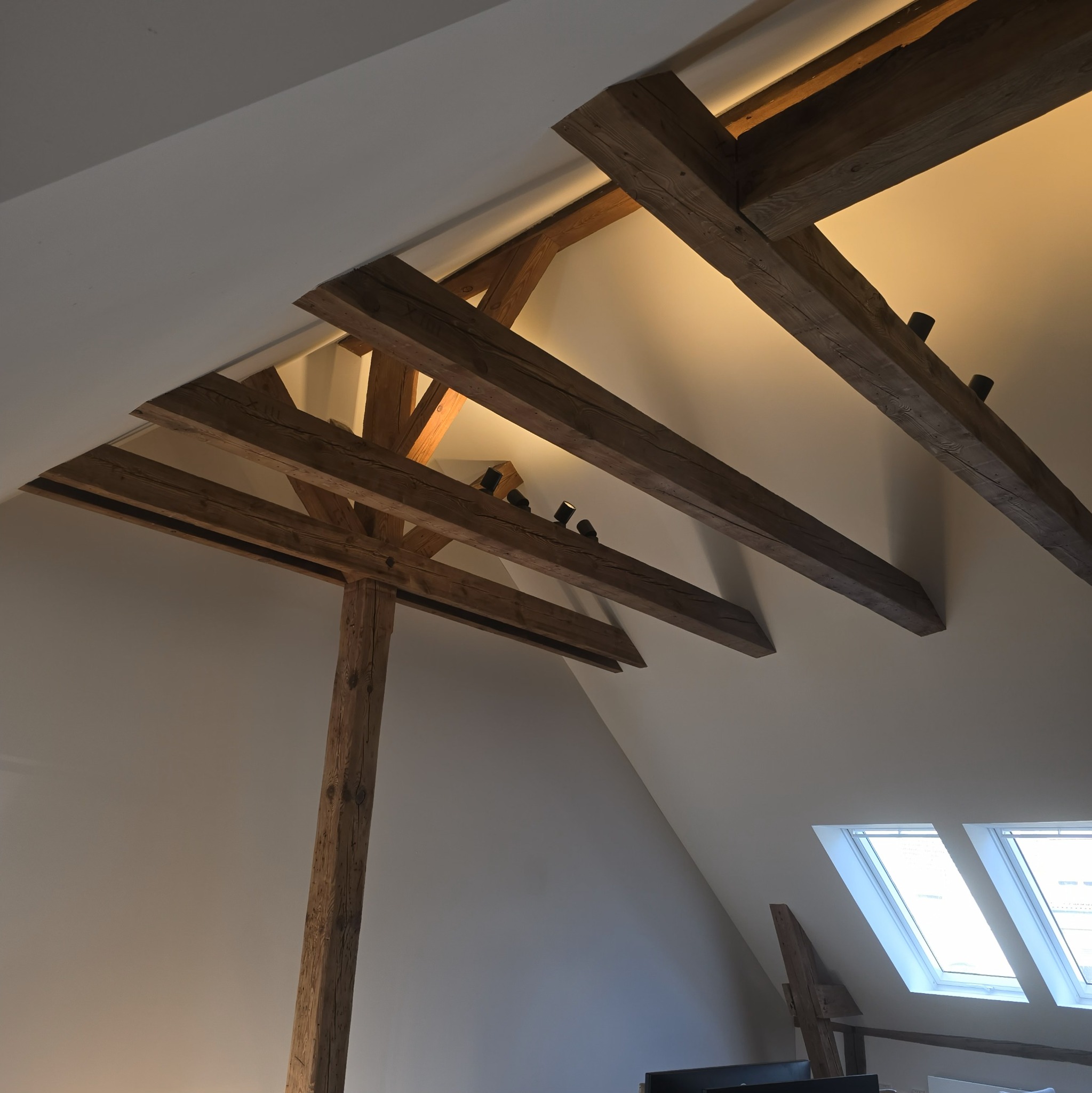 Drewniana konstrukcja stropu z oświetleniem punktowym w nowoczesnym wnętrzu poddasza z oknami dachowymi. Widok z dołu na belki i lampy.