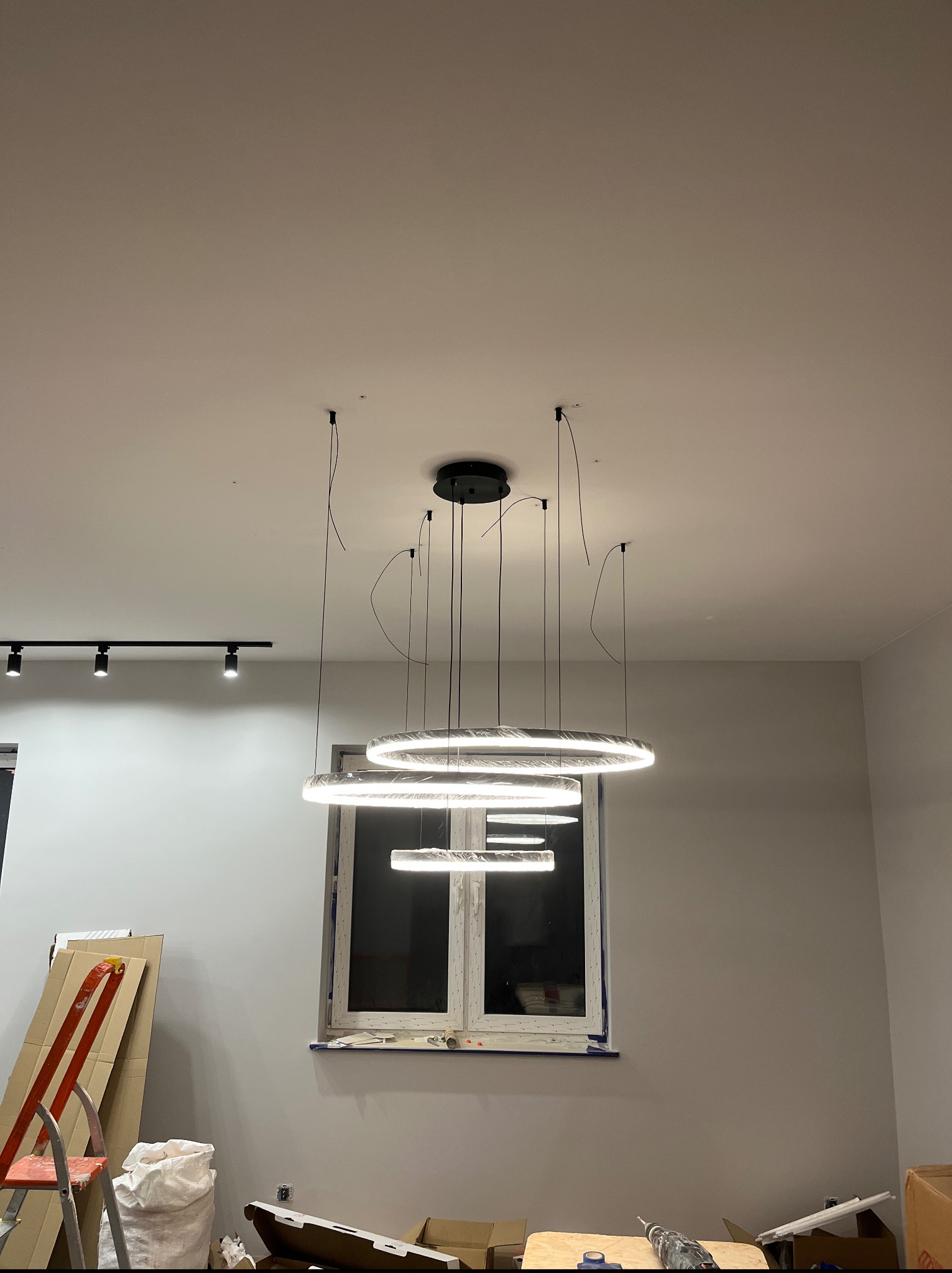 Montaż nowoczesnej lampy sufitowej z okrągłymi elementami LED w nowym wnętrzu. Widoczne narzędzia i drabina, co sugeruje etap wykończeniowy.