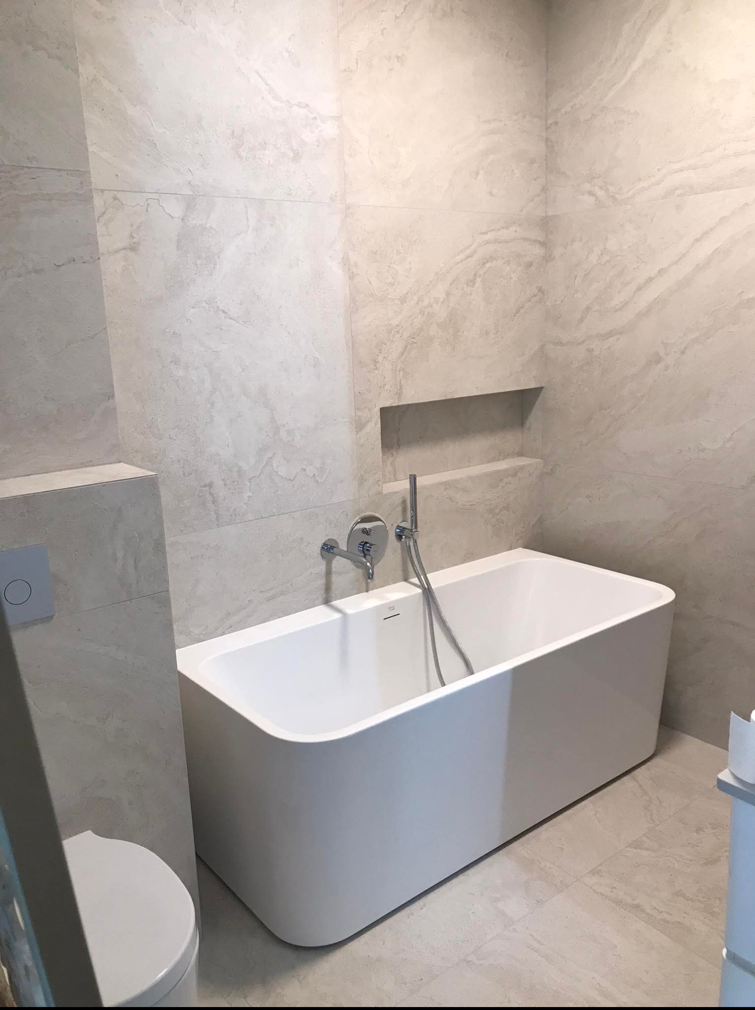 Nowoczesna łazienka w Grójcu z wanną prostokątną, armaturą i płytkami imitującymi marmur. Wnęka w ścianie dodaje elegancji.