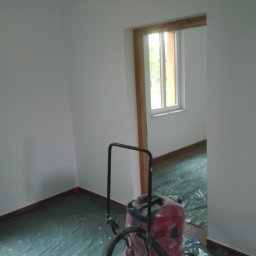 UKR-POL BUD Yurii Herchuk - Przygotowanie do malowania: Pokój zabezpieczony folią malarską, widoczny odkurzacz przemysłowy Hilti. Świeżo pomalowane ściany na biało, drewniane listwy przypodłogowe.