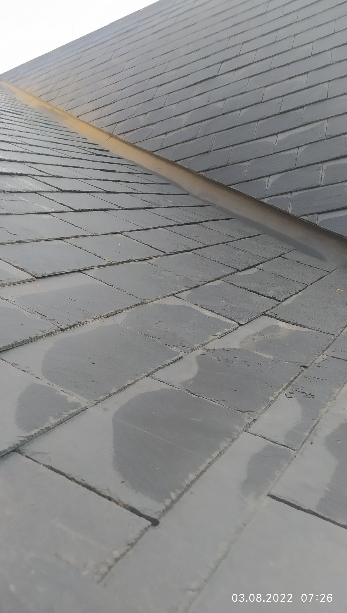 Szary dach pokryty łupkiem, widoczny pod kątem. Na dachu widoczny element odprowadzający wodę. Data i godzina wykonania zdjęcia w prawym dolnym rogu.
