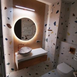 DS Wykończenia Dariusz Szczygłowski - Nowoczesna łazienka z okrągłym lustrem LED, umywalką w kształcie muszli i wzorem lastryko na ścianach i podłodze. Minimalistyczny design z akcentami miedzianymi.