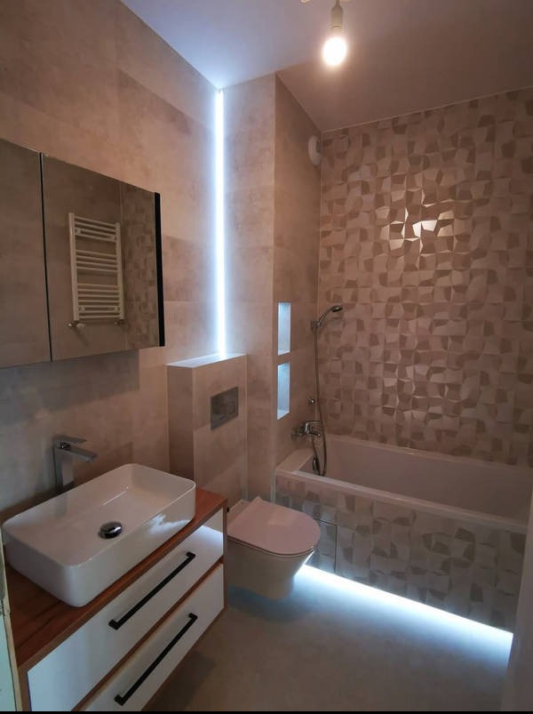 Nowoczesna łazienka z podświetleniem LED: umywalka nablatowa, geometryczne płytki 3D, zabudowana toaleta. Minimalistyczny design z akcentami światła.