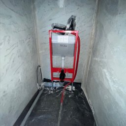 Marciniak NTG - Stelaż podtynkowy WC marki Tece w trakcie montażu, widoczne rury doprowadzające wodę i odpływ. Ściany surowe, w trakcie wykończenia. Podłoga zabezpieczona folią.