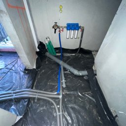 ELIASZ MARCINIAK NOWOCZESNE TECHNOLOGIE GRZEWCZE - Instalacja filtrów wody z rurami w pomieszczeniu z folią ochronną na podłodze. Widoczne elementy instalacji hydraulicznej i filtrów.