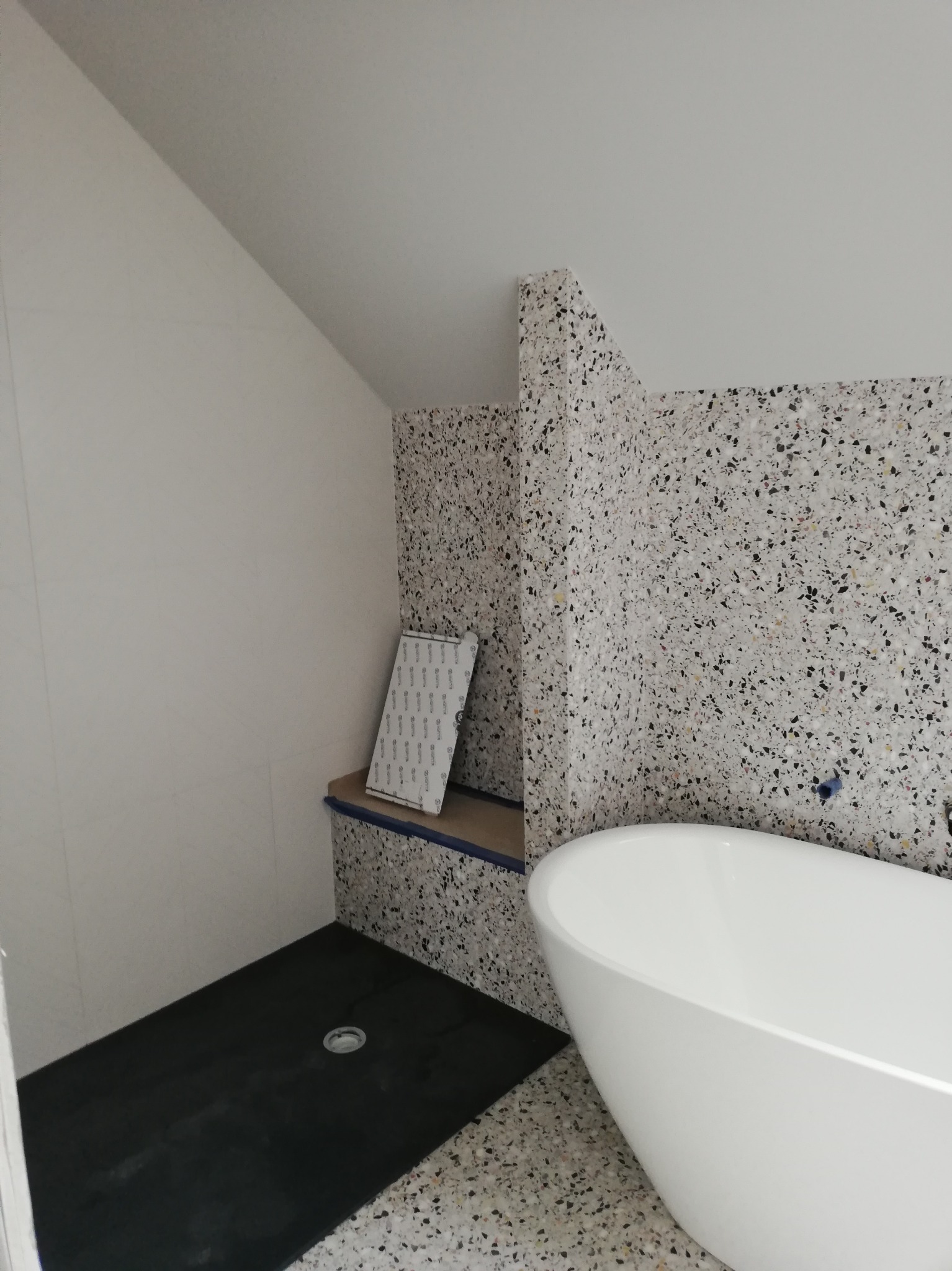 Nowoczesna łazienka na poddaszu z wanną wolnostojącą i ścianami wykończonymi mozaiką lastryko. Czarny brodzik i białe ściany tworzą kontrast.