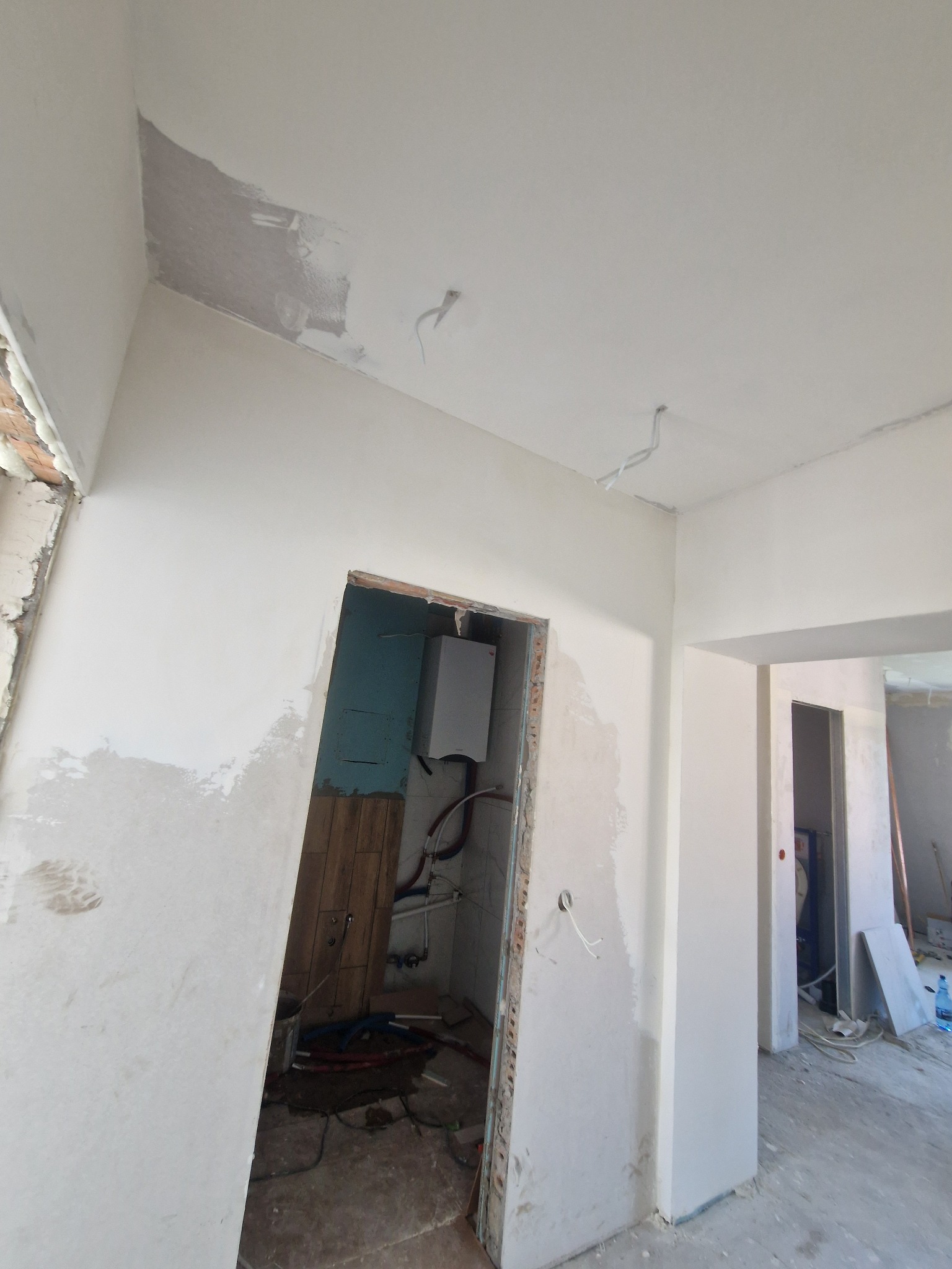 Wnętrze w trakcie prac wykończeniowych: ściany po szpachlowaniu, widoczne instalacje w łazience, surowe ościeżnice. Prace przygotowawcze przed malowaniem.