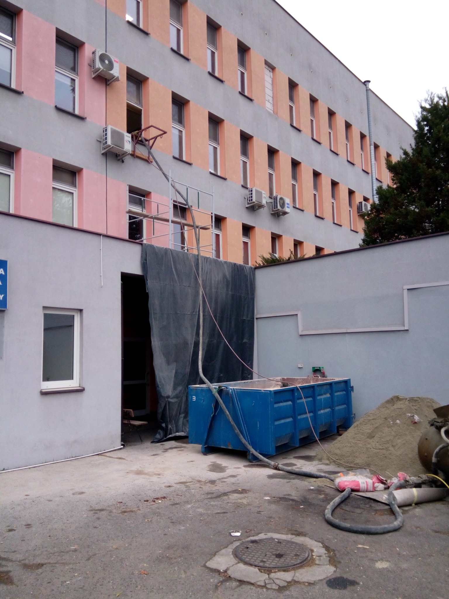 Ocieplanie budynku w Pawłowicach: kontener, rusztowanie i wąż do natrysku izolacji. Prace elewacyjne w toku, widoczny fragment ocieplonej ściany.