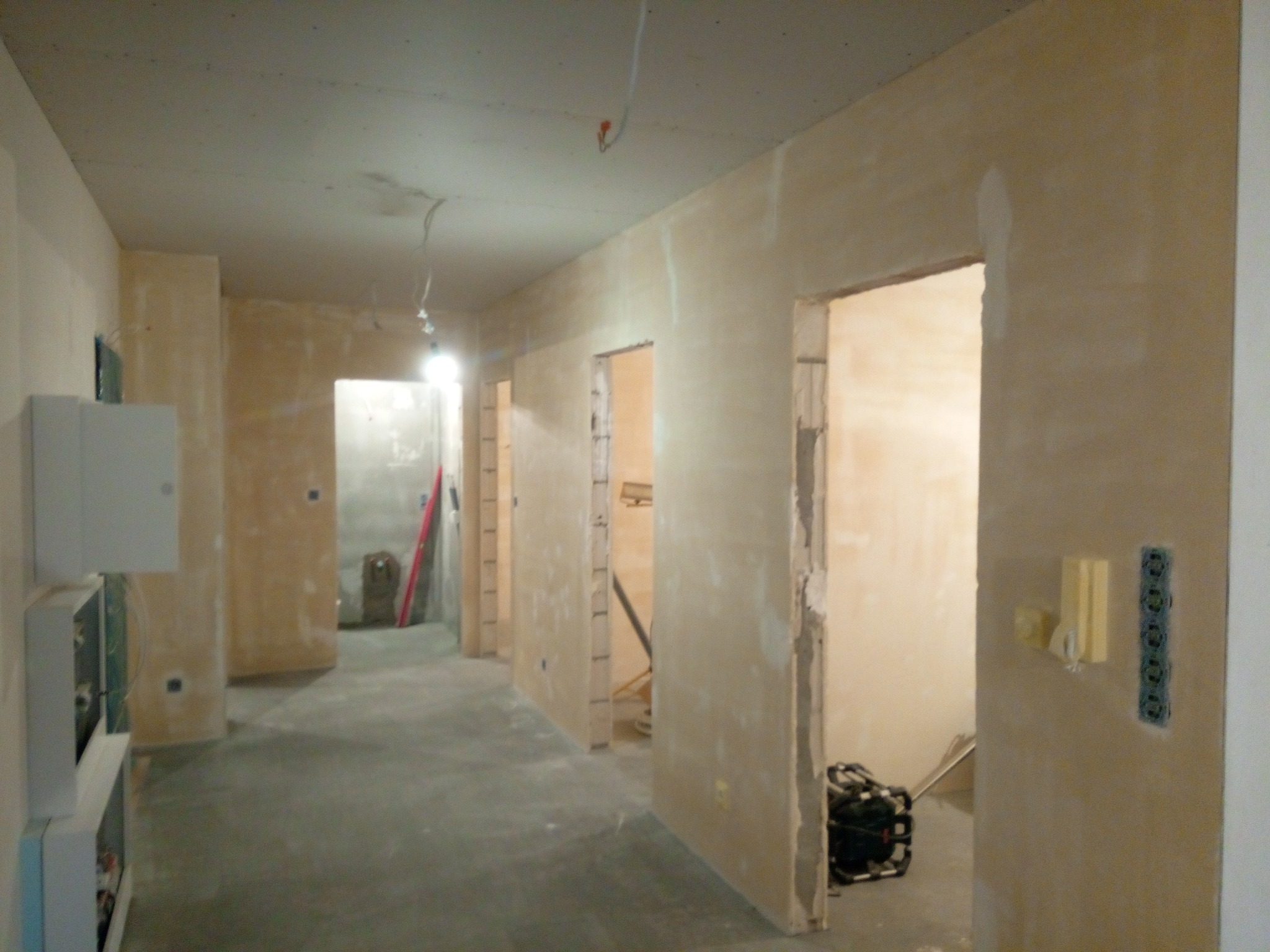 Wnętrze w trakcie prac wykończeniowych: ściany przygotowane pod malowanie, widoczne gładzie i instalacje elektryczne. Surowy beton na podłodze, brak wykończenia.