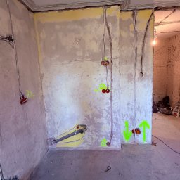 Dobra Faza - Wnętrze w trakcie remontu z widocznymi przewodami elektrycznymi i puszkami instalacyjnymi w ścianach. Żółte oznaczenia na ścianach. Widoczne kable ułożone wzdłuż sufitu.