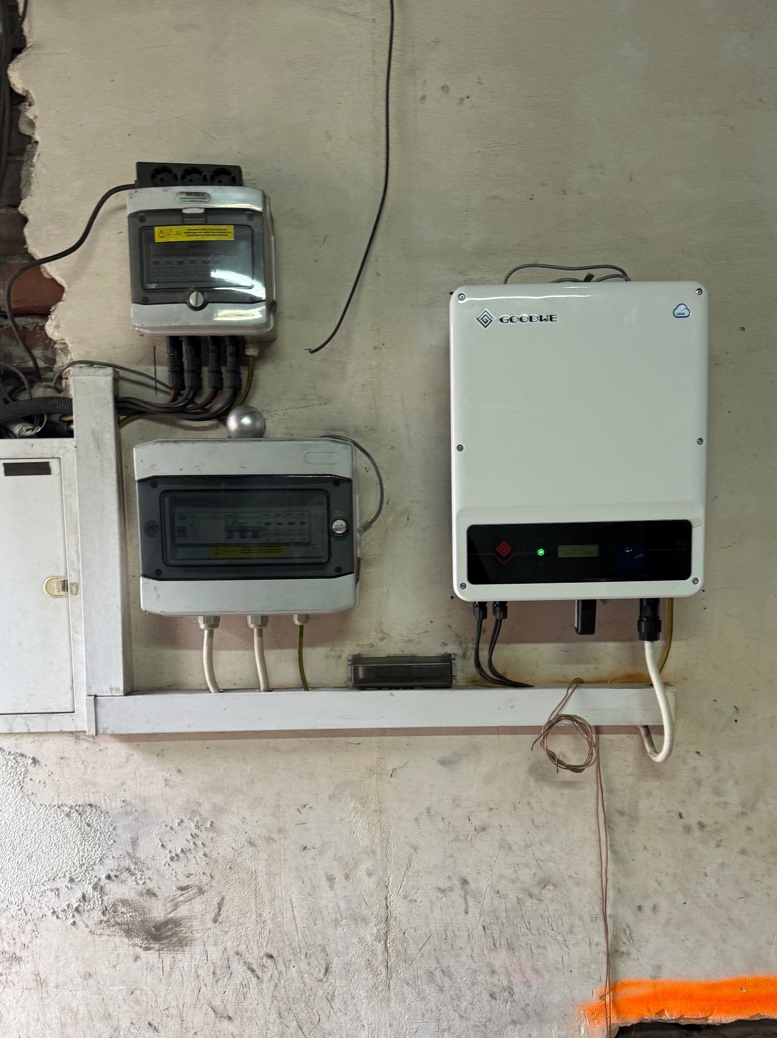 Zamontowana skrzynka elektryczna, rozdzielnica i falownik Goodwe na ścianie z widocznymi przewodami. Elementy instalacji elektrycznej wewnątrz budynku.