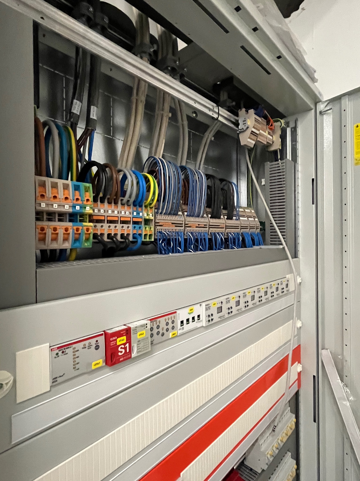 Rozdzielnica elektryczna z widocznymi przewodami, złączkami i elementami sterującymi. Kolorowe kable uporządkowane wewnątrz szafy sterowniczej.