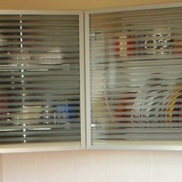 Ruslan Alyshov - Dwa okna szafki kuchennej z poziomymi żaluzjami, częściowo zasłonięte matową folią, ukazujące zawartość szafki w tle. Jasne ramy okien.