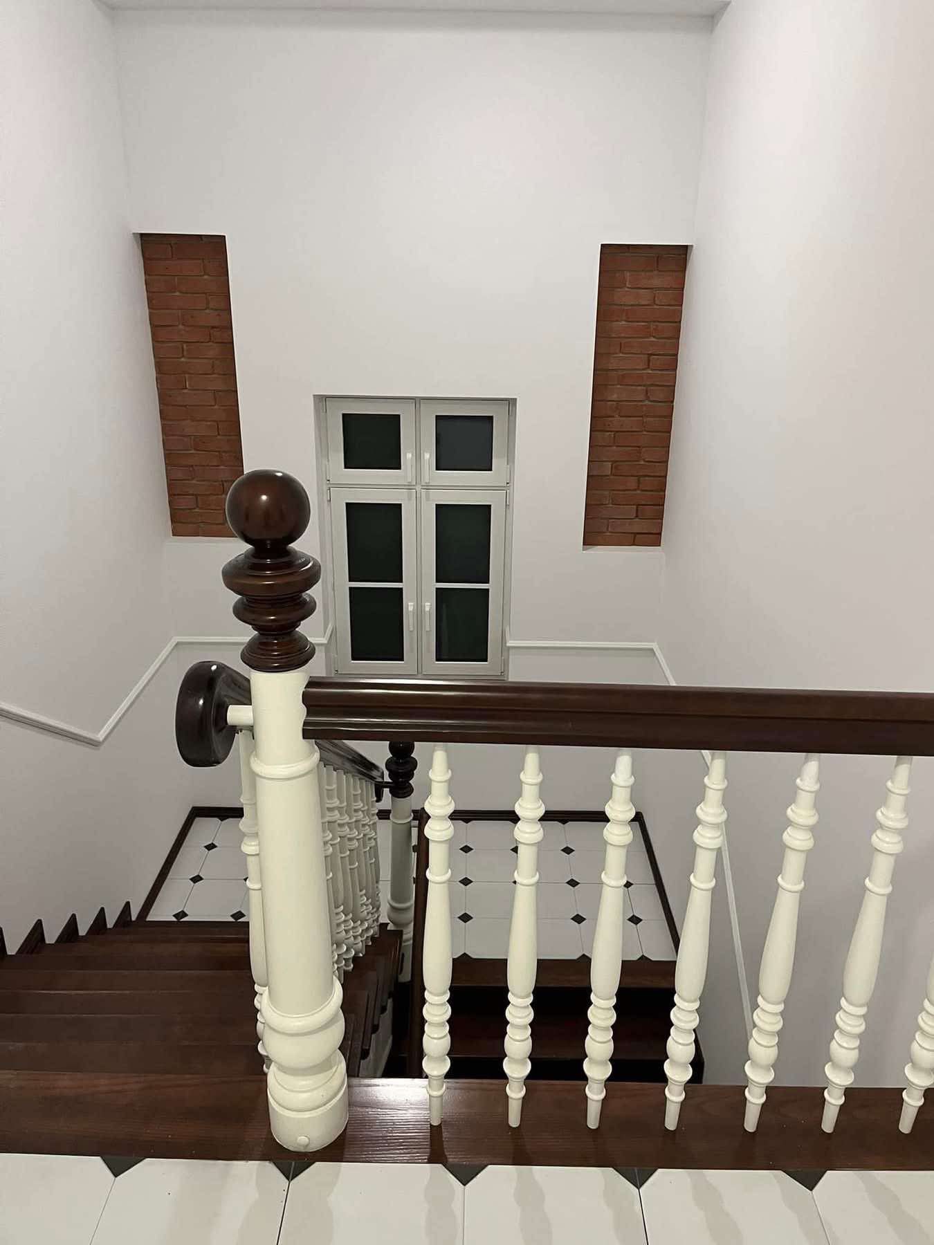 Klatka schodowa z drewnianymi schodami i białą balustradą. Na ścianie dekoracyjne wstawki z cegły i okno. Podłoga wyłożona biało-czarną mozaiką.