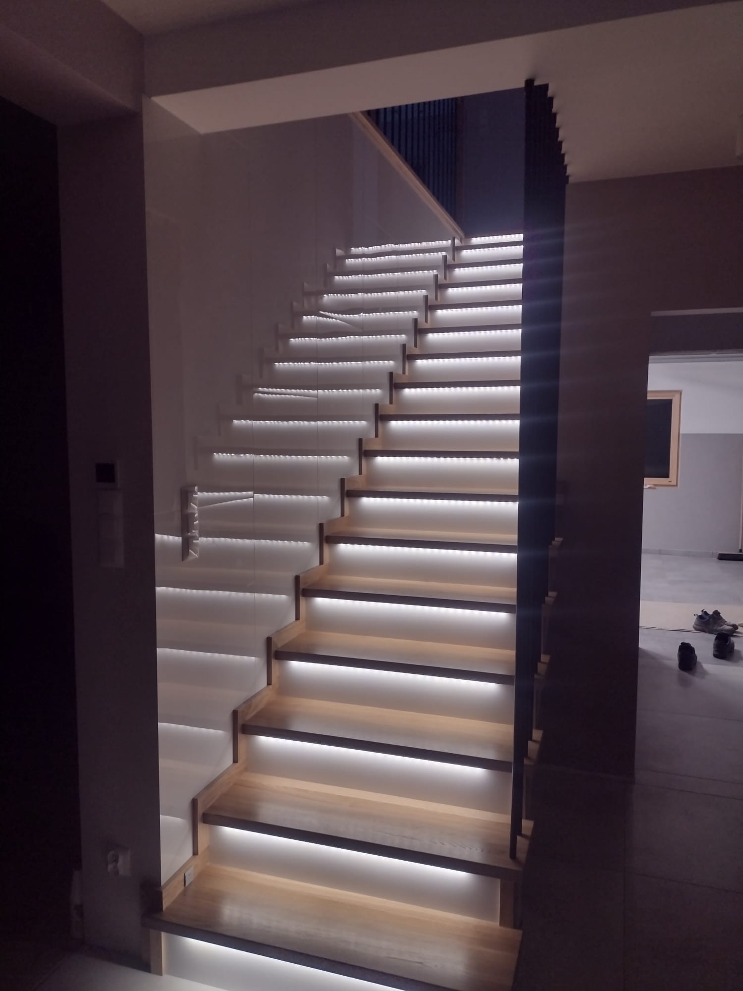 Nowoczesne schody drewniane z podświetleniem LED, widok z dołu. Minimalistyczny design, jasne drewno, subtelne oświetlenie, ciemne elementy konstrukcyjne.