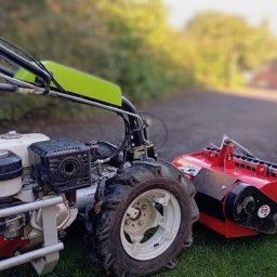 Ogrody po Naszymu - Glebogryzarka separacyjna, z bliska, na trawie w Rybniku. Czerwony agregat roboczy, białe felgi, zielony element. Sprzęt do przygotowania podłoża pod trawnik.
