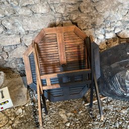 DS laser cleaning - Drewniany, ośmiokątny stół z krzesłami w trakcie renowacji, częściowo pomalowany na czarno, oparty o kamienną ścianę w piwnicy.