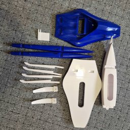 Mateusz Wujak - Elementy modelu trimaranu, wydrukowane w 3D, w kolorach białym i niebieskim, rozłożone na szarym tle. Widoczne ślady warstw wydruku.