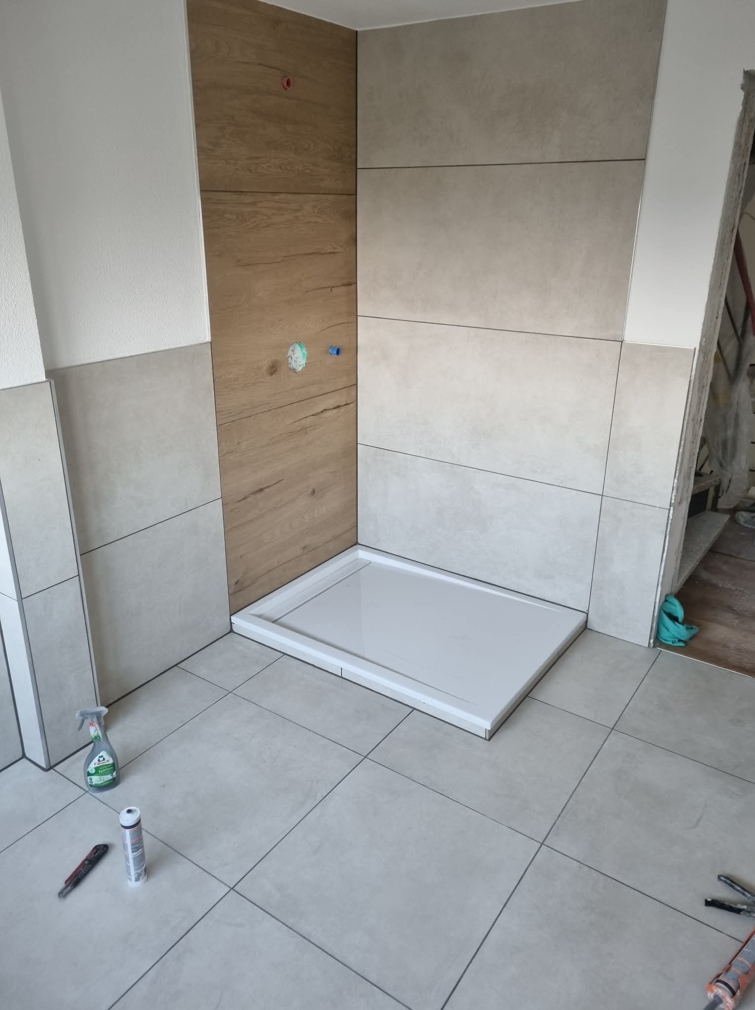 Montaż brodzika w łazience z wykończonymi płytkami imitującymi drewno i szare płytki. Widoczne narzędzia i chemia budowlana na podłodze.