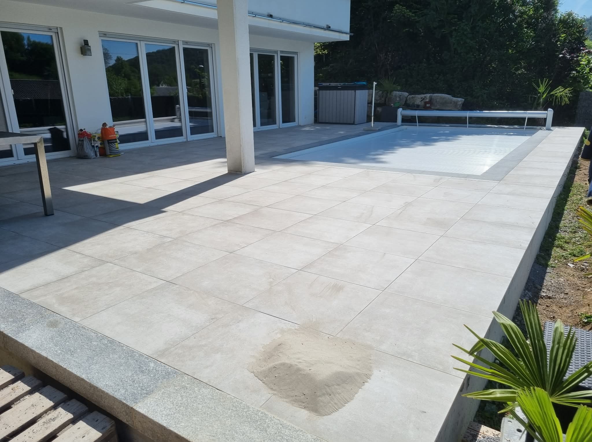 Jasne, kwadratowe płytki na tarasie z basenem i jacuzzi. Widoczne narzędzia i materiały budowlane. Minimalistyczny styl, nowoczesne wykończenie.