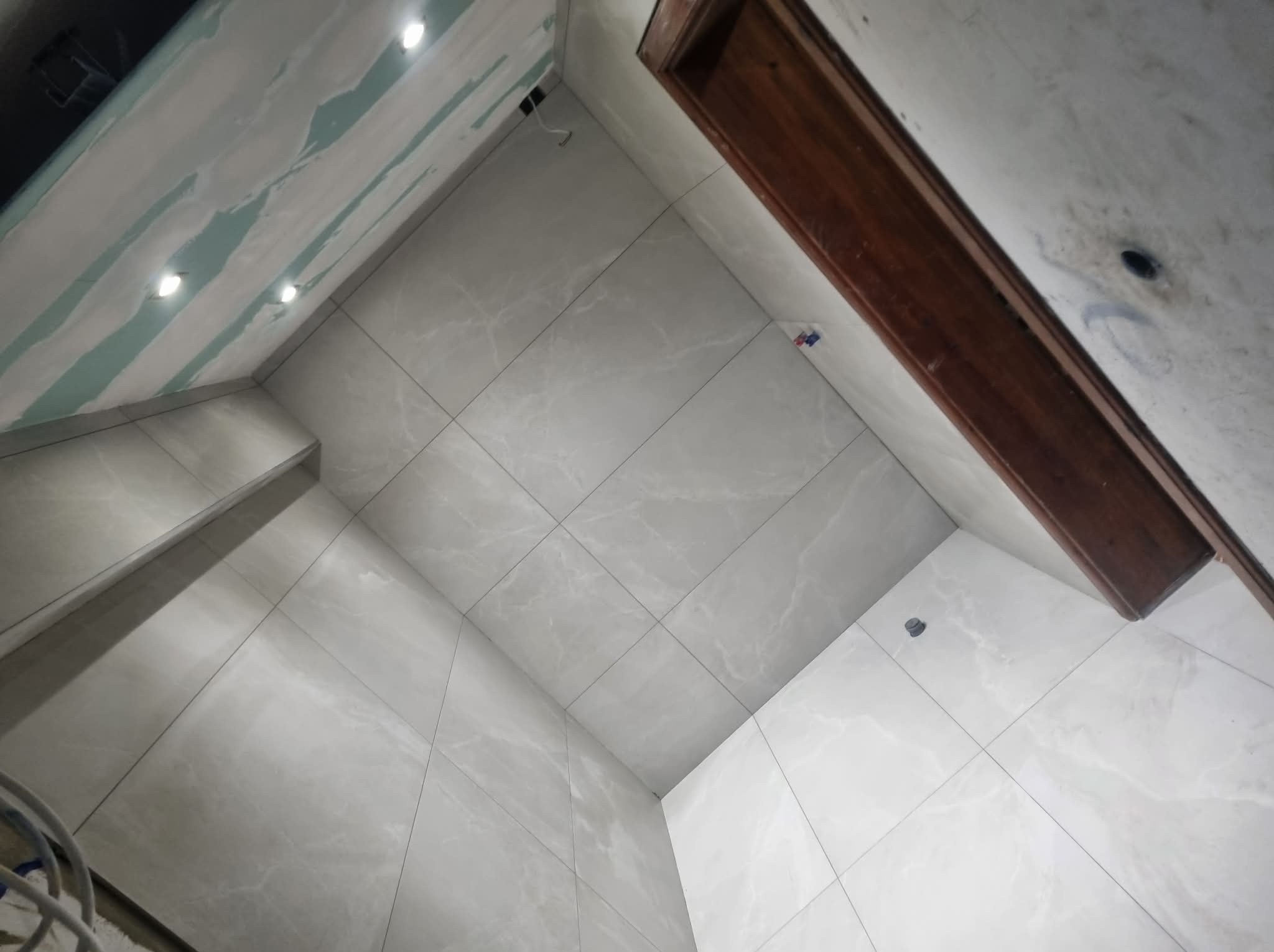 Wykończona łazienka w Sidzinie z szarymi płytkami imitującymi marmur na ścianach i suficie. Widoczne oświetlenie punktowe i fragment drewnianej ramy drzwi.