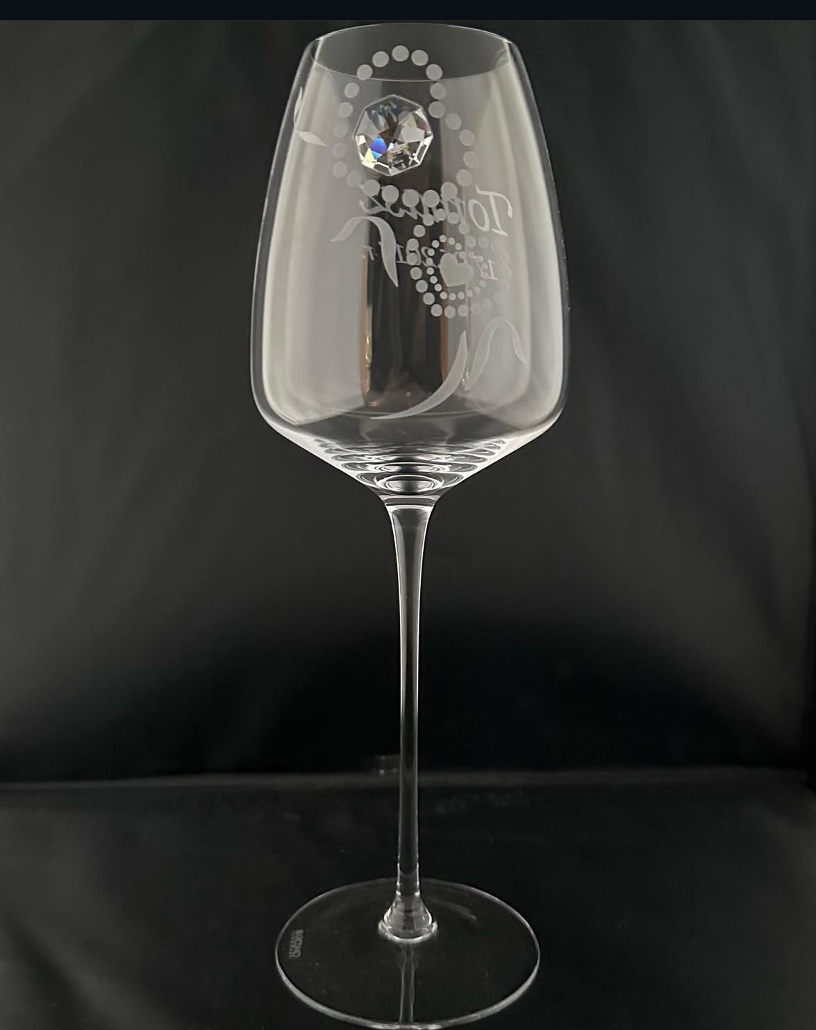 Elegancki kieliszek do wina z grawerowanym wzorem i kryształkiem, na czarnym tle. Precyzyjne zdobienie szkła, wysoka nóżka, subtelne detale.