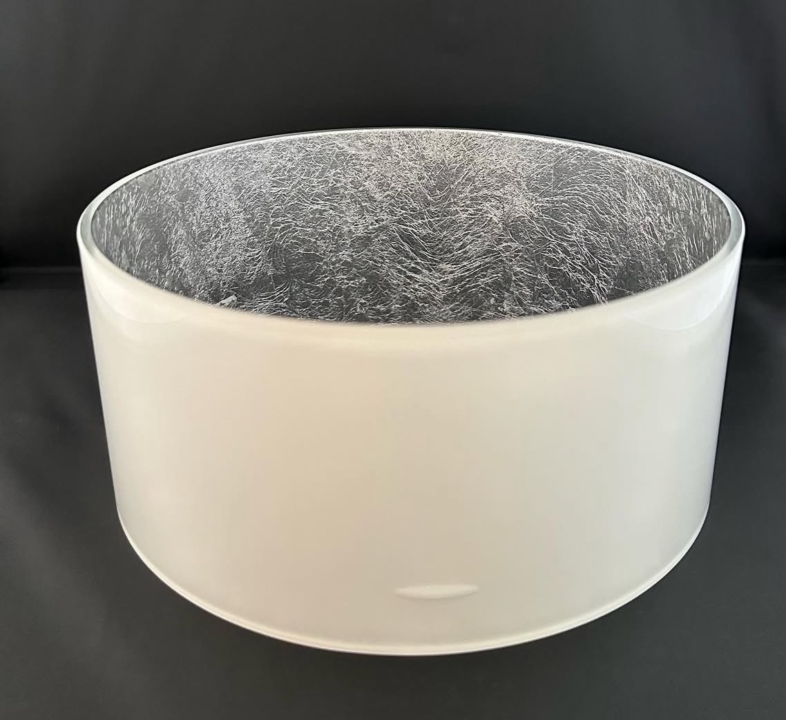 Okrągły, biały klosz lampy z delikatną, srebrzystą fakturą wewnątrz, na czarnym tle. Minimalistyczny design, gładka powierzchnia, subtelne światło odbijające się od wnętrza.