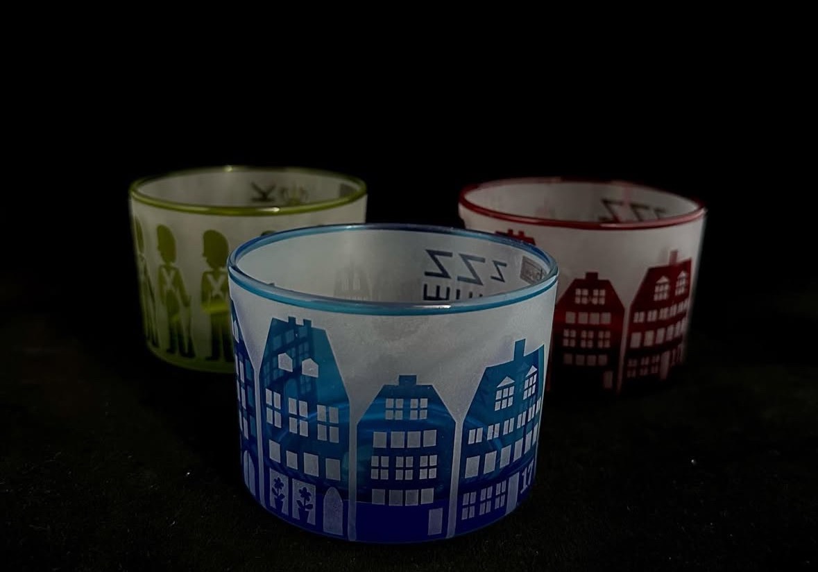 Szklane świeczniki z motywami: niebieskie kamieniczki, zieloni żołnierze, czerwone domki. Różne wzory na każdym, na czarnym tle. Dekoracyjne szkło.