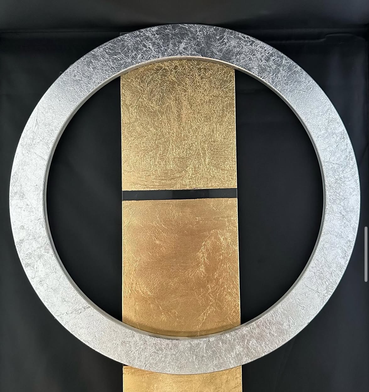 Abstrakcyjna kompozycja: srebrny okrąg na tle pionowego, złotego prostokąta z czarnym pasem, na czarnym tle. Unikalna faktura i gra kolorów.