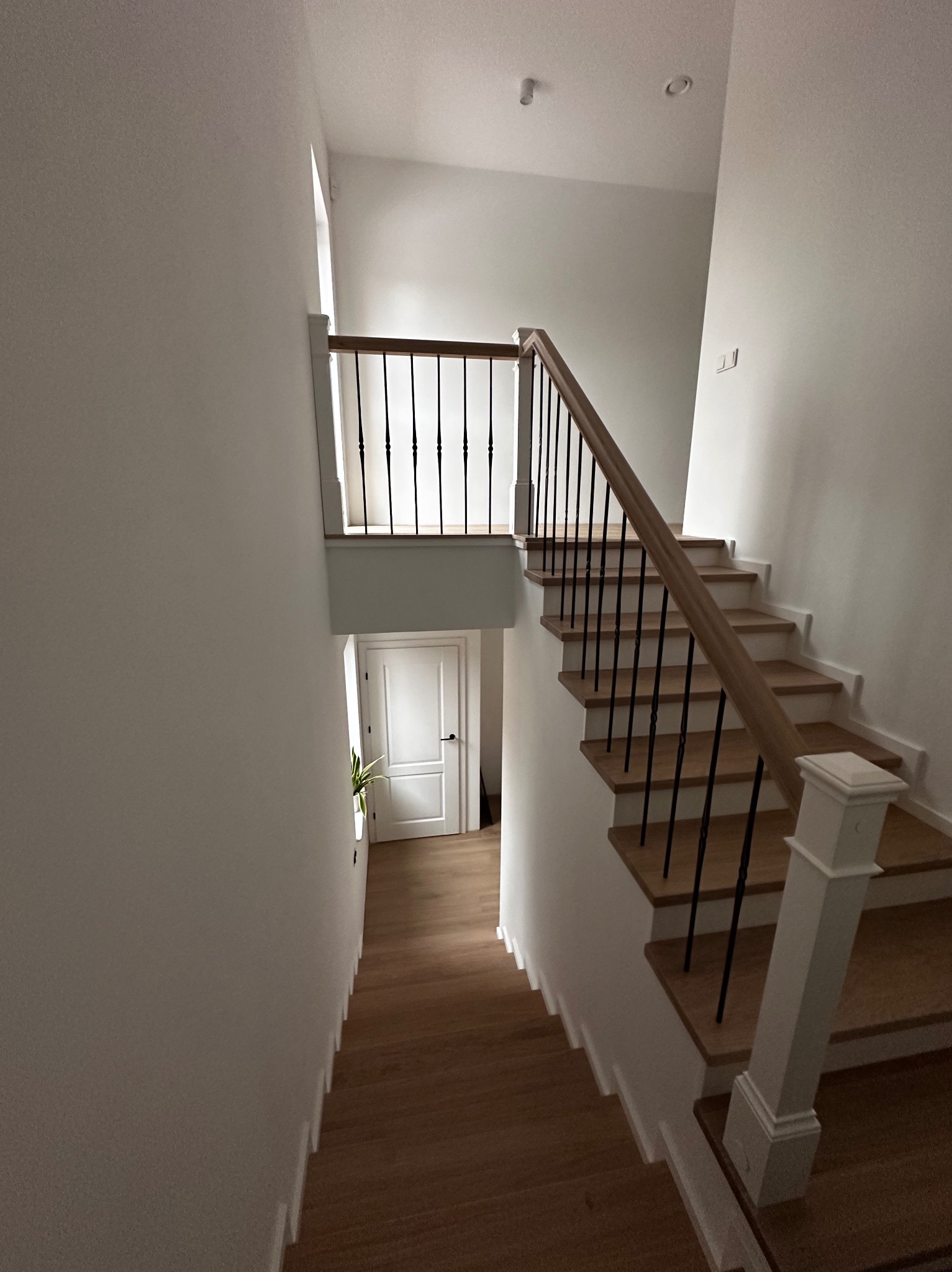 Jasne schody z drewnianymi stopniami i czarną, metalową balustradą w nowoczesnym wnętrzu. Widok z góry na dół, z akcentem na minimalistyczny design.