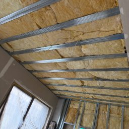 K.E.M remonty i wykończenia - Ocieplenie poddasza wełną mineralną, widoczne metalowe profile konstrukcyjne. Okno zabezpieczone folią malarską. Prace wykończeniowe w trakcie realizacji.