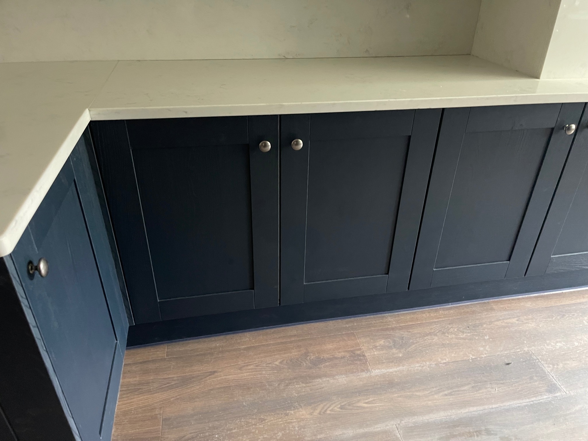 Granatowe szafki kuchenne z jasnym blatem i drewnianą podłogą. Widoczne srebrne uchwyty. Ujęcie z dołu, podkreślające detale wykończenia.