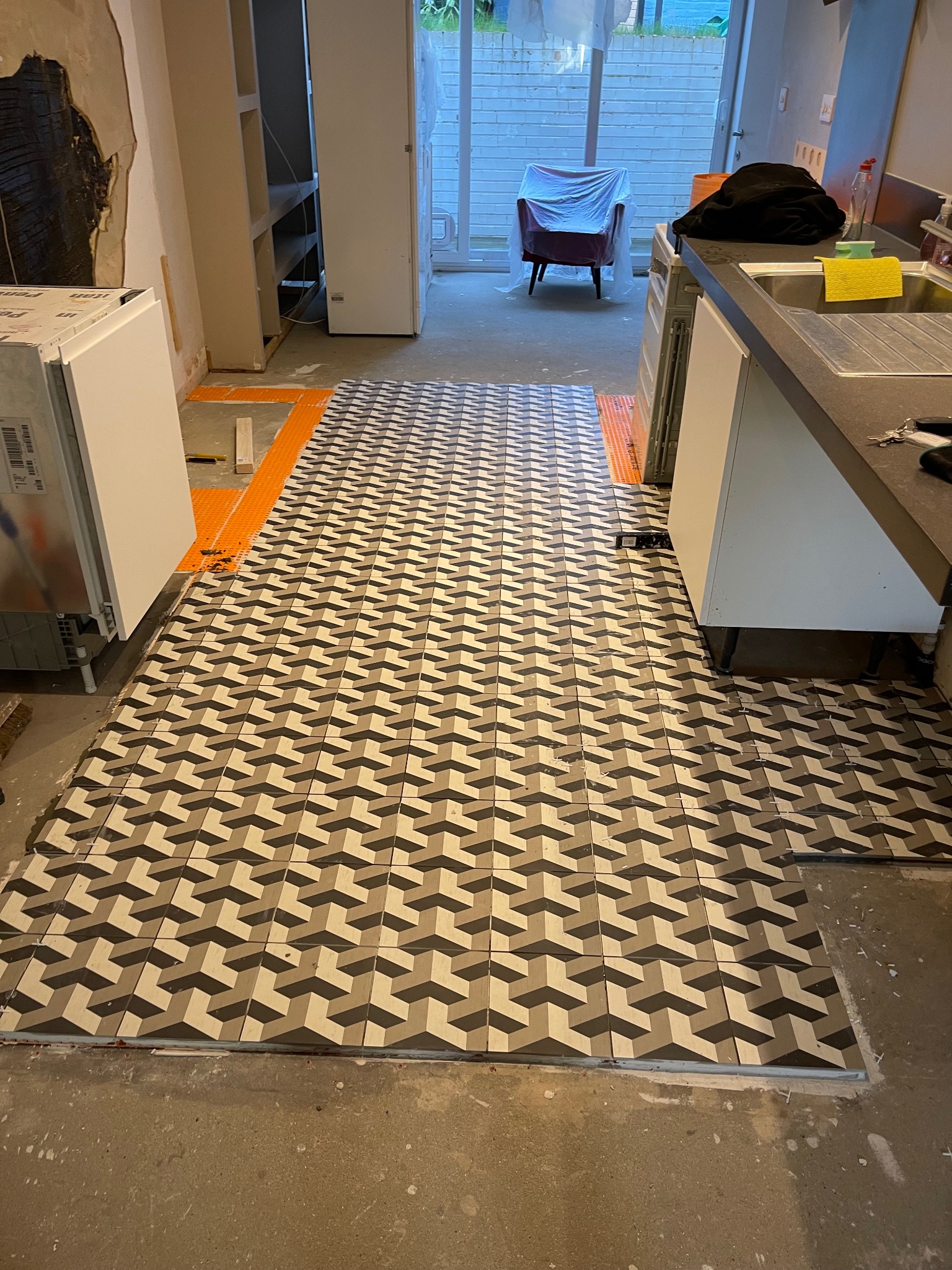 Ułożona podłoga z płytek o geometrycznym wzorze 3D w trakcie remontu kuchni. Widoczne fragmenty niezakończonej podłogi i przygotowane podłoże.