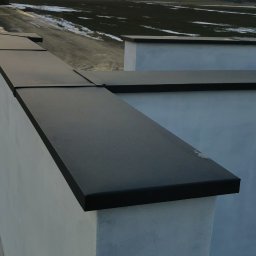 Be-Gro Dachy - Nowoczesne obróbki blacharskie na murze oporowym w kolorze antracytowym, z widokiem na pole i zachodzące słońce. Estetyczne wykończenie.