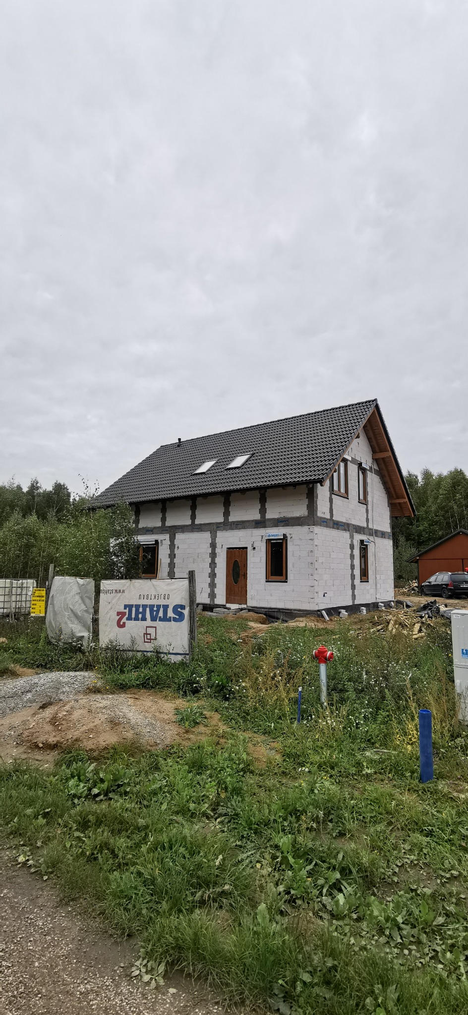 Dom jednorodzinny w stanie surowym zamkniętym z ciemną dachówką w Gniezno. Widoczne okna dachowe i drewniane elementy konstrukcji dachu.